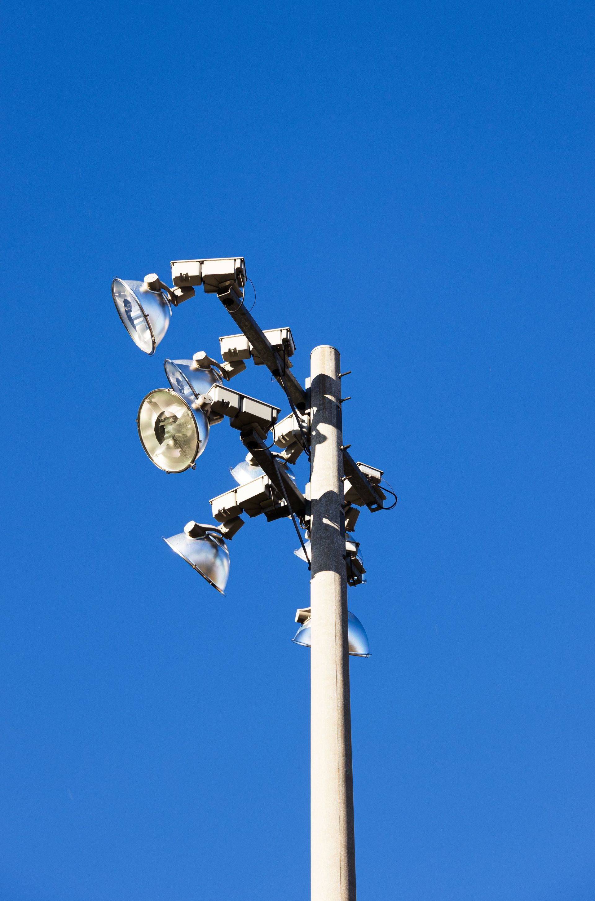 Cluster of stadium floodlights on a white pole against a bright blue sky