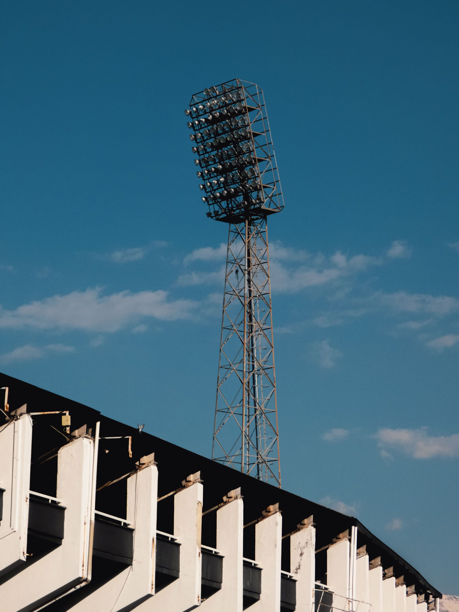 Stadium floodlight tower above a rooftop against a blue sky