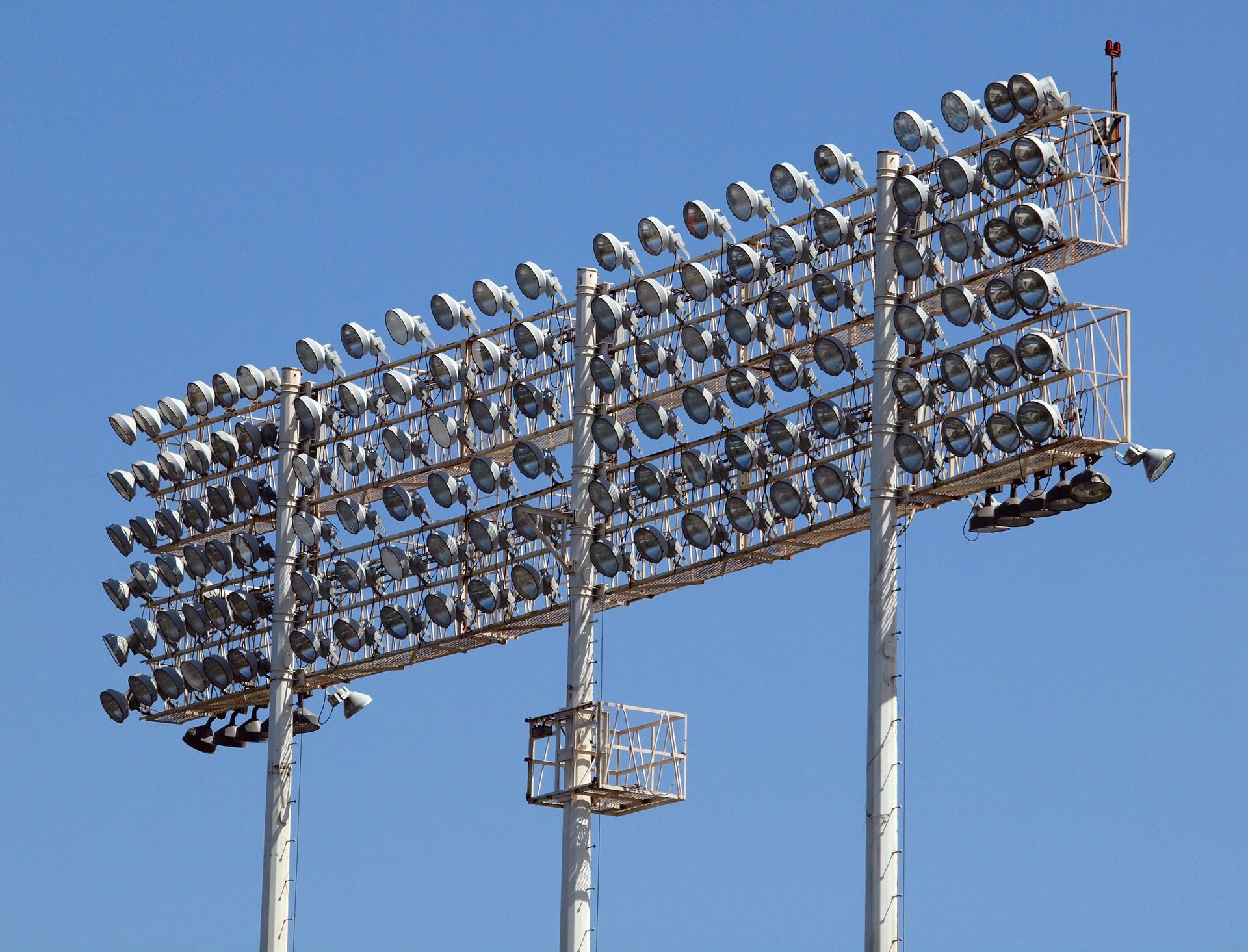 Bank of stadium floodlights on steel poles against a clear blue sky