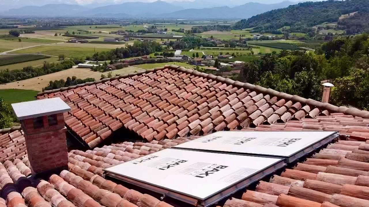 Tettoia con tegole in terracotta e pannelli solari con vista su una verde vallata rurale e sulle colline in lontananza.