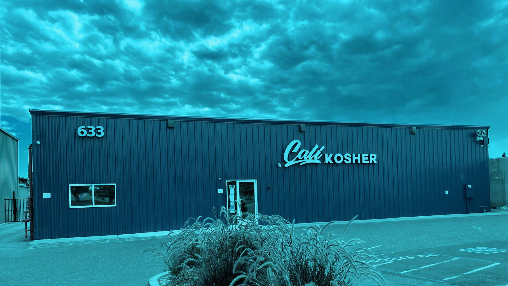 Exterior of Cali Kosher’s Oakdale dispensary, featuring a dark blue facade, storefront sign, and parking area.