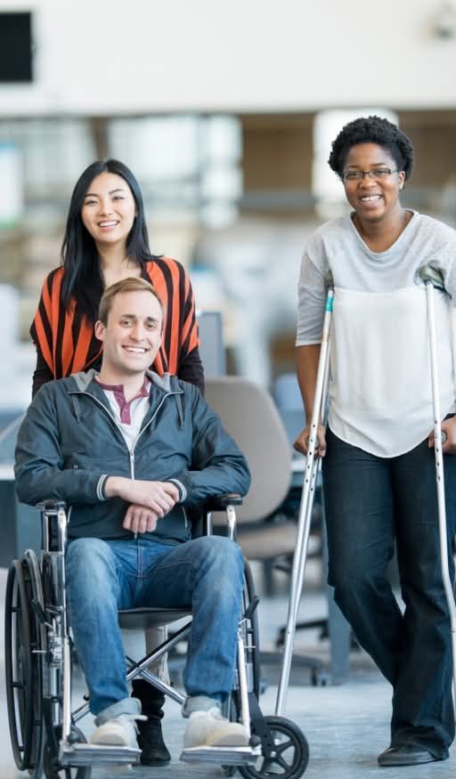 A man in a wheelchair is standing next to two women with crutches.