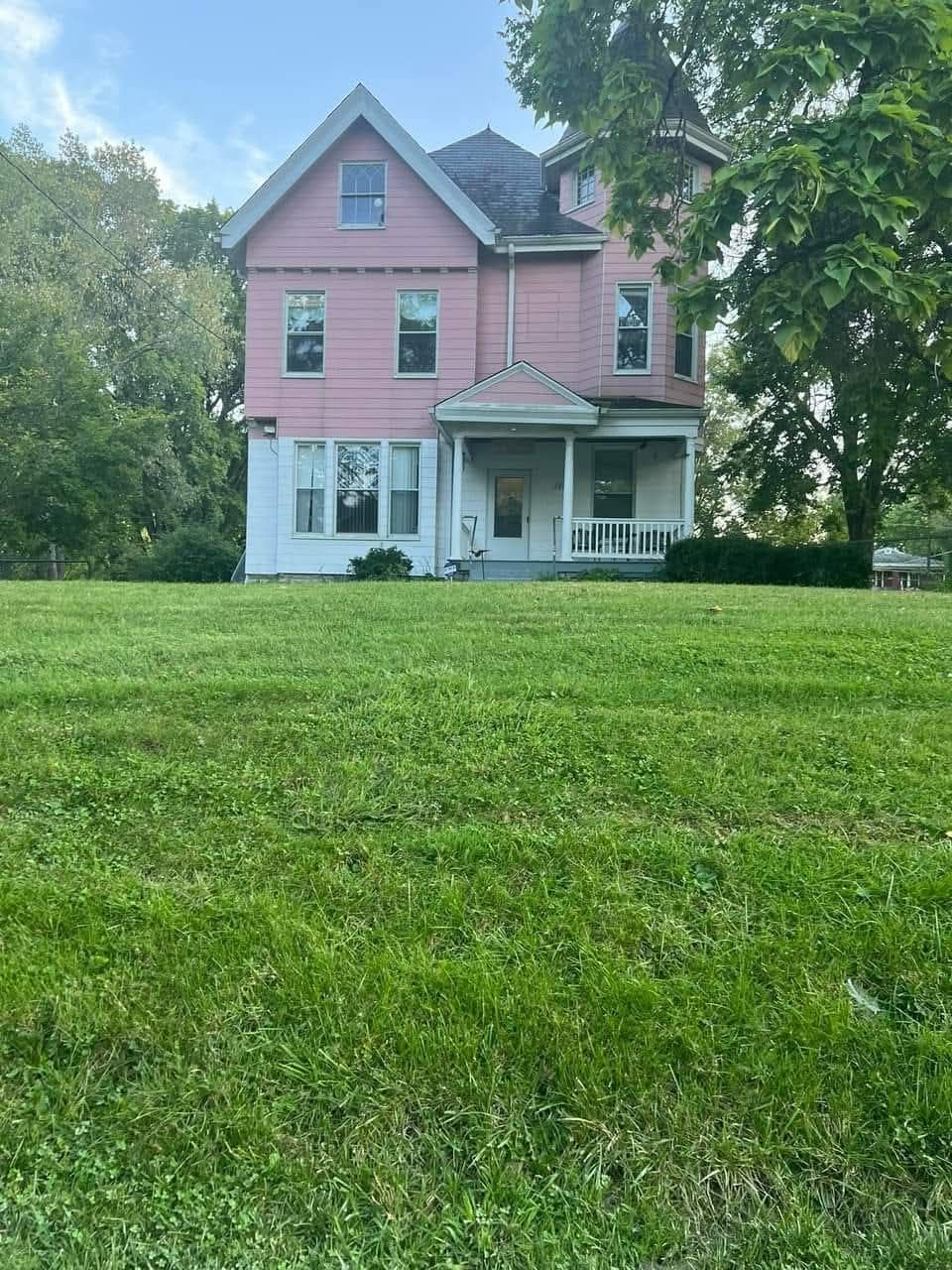 A large pink house sits in the middle of a lush green field