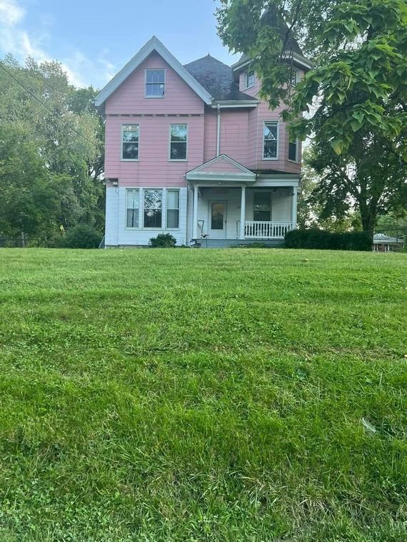 A large pink house sits in the middle of a lush green field