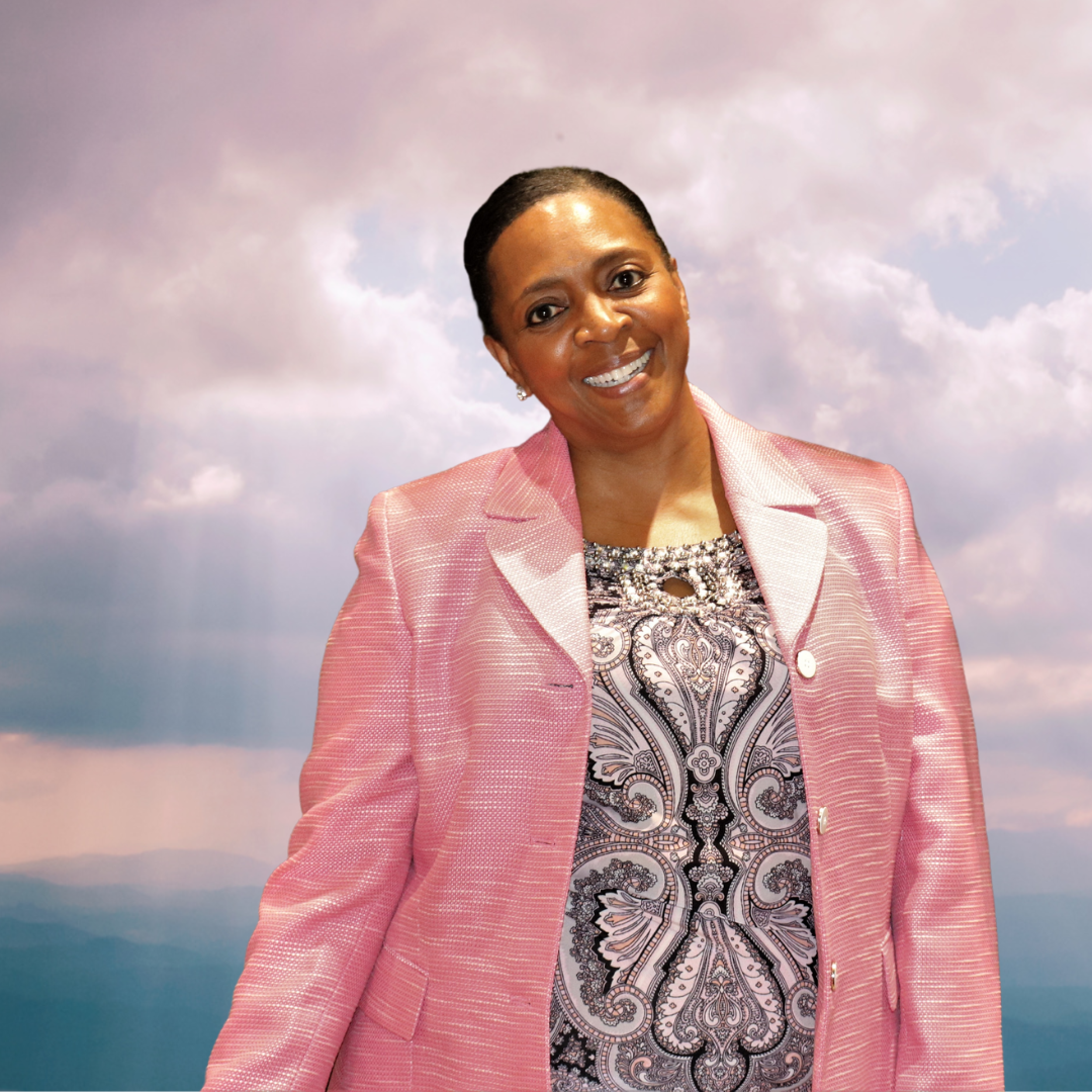 A woman wearing a pink jacket and a paisley shirt is smiling
