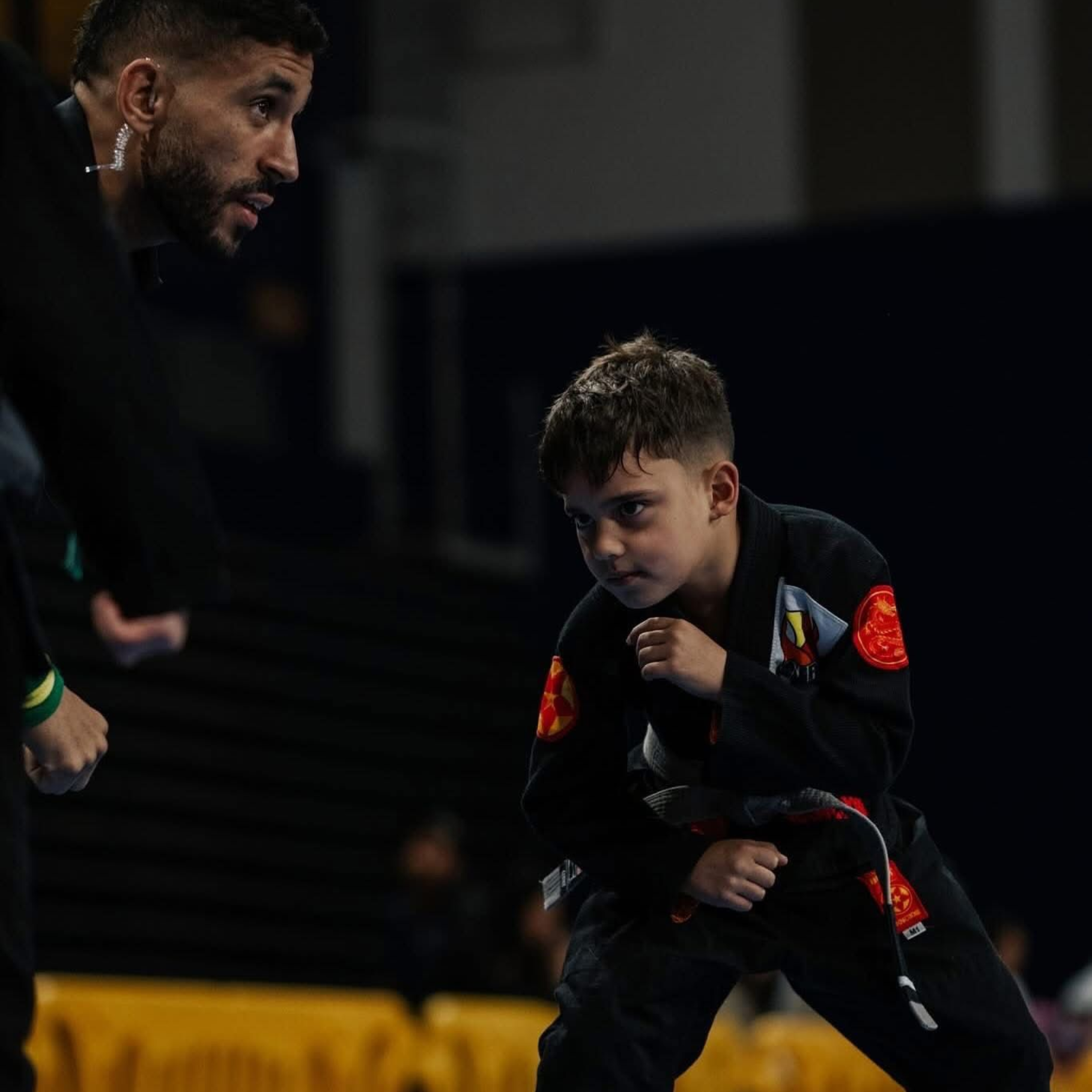 Two boys in black martial arts uniforms practice grappling on a mat.