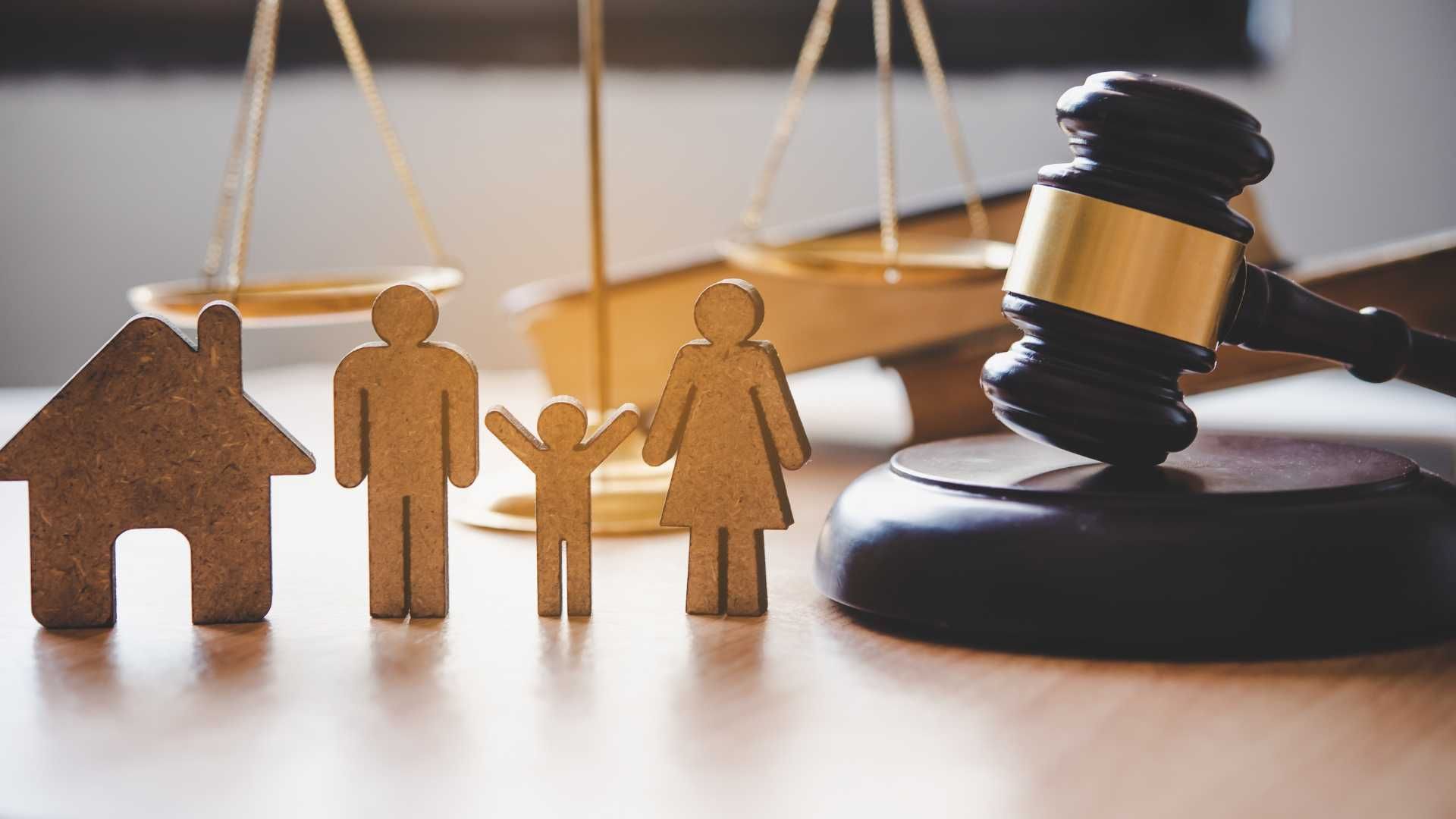 a wooden family , house , scales of justice and a judge 's gavel on a table .