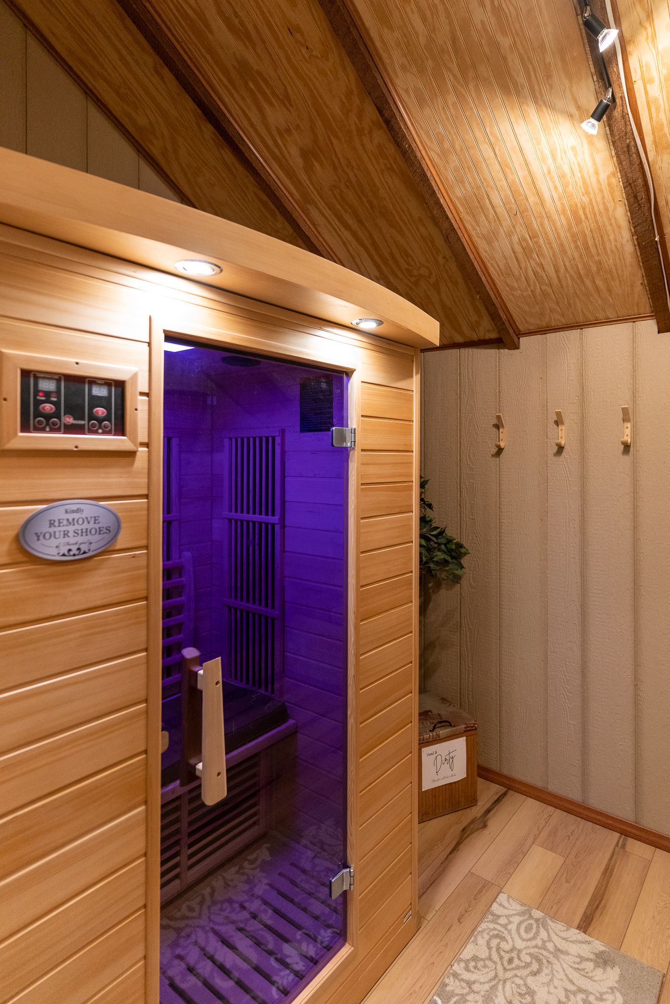 Wood-paneled sauna interior with glass door, purple light inside, and a bench along the right wall