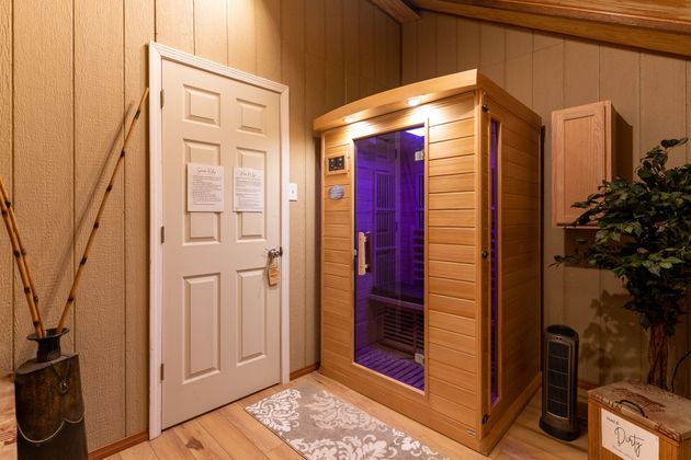 Home sauna room with a wooden infrared sauna, white door, and warm wood-paneled walls.