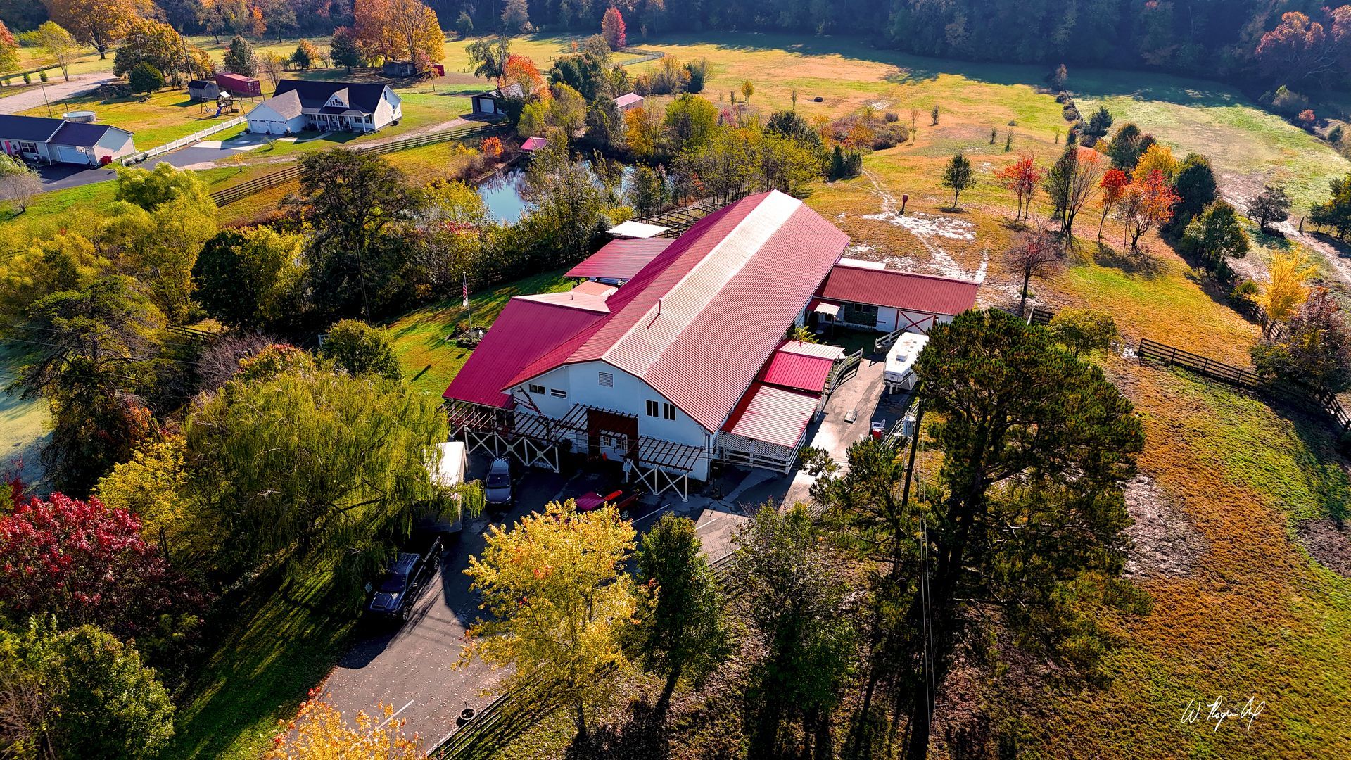 Aerial view of a red-roofed farmhouse surrounded by trees and autumn fields.