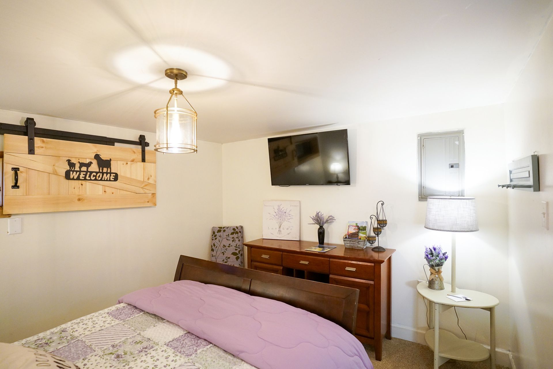 Cozy bedroom with a bed, dresser, wall-mounted TV, and soft lavender accents