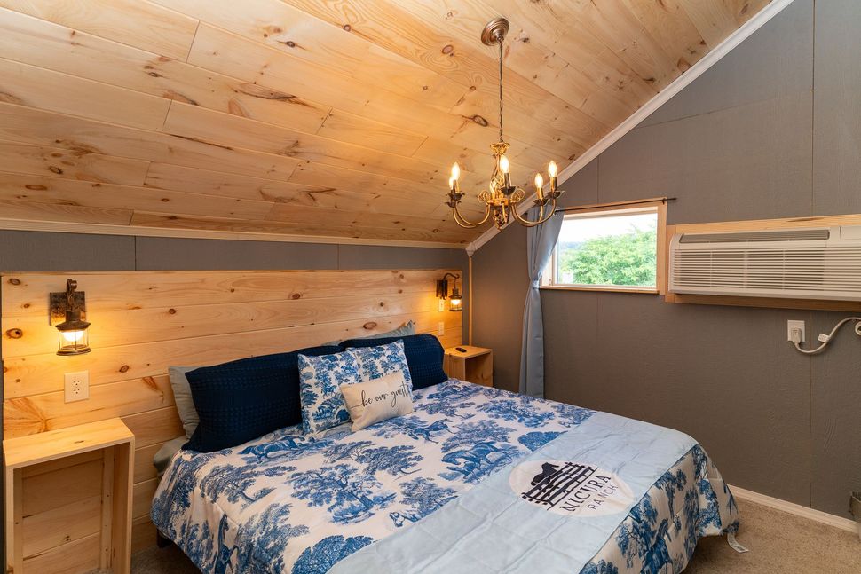 Cozy bedroom with blue floral bedding, wood-paneled ceiling, and window AC unit