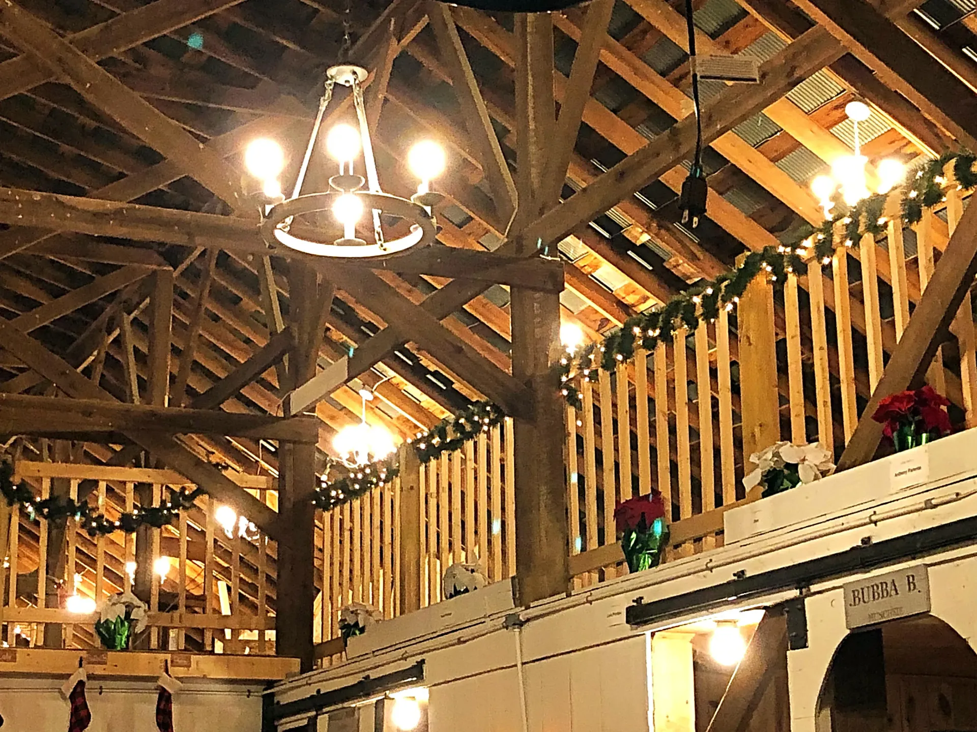 Rustic barn interior with exposed wooden beams, warm hanging lights, and loft railings adorned with flowers