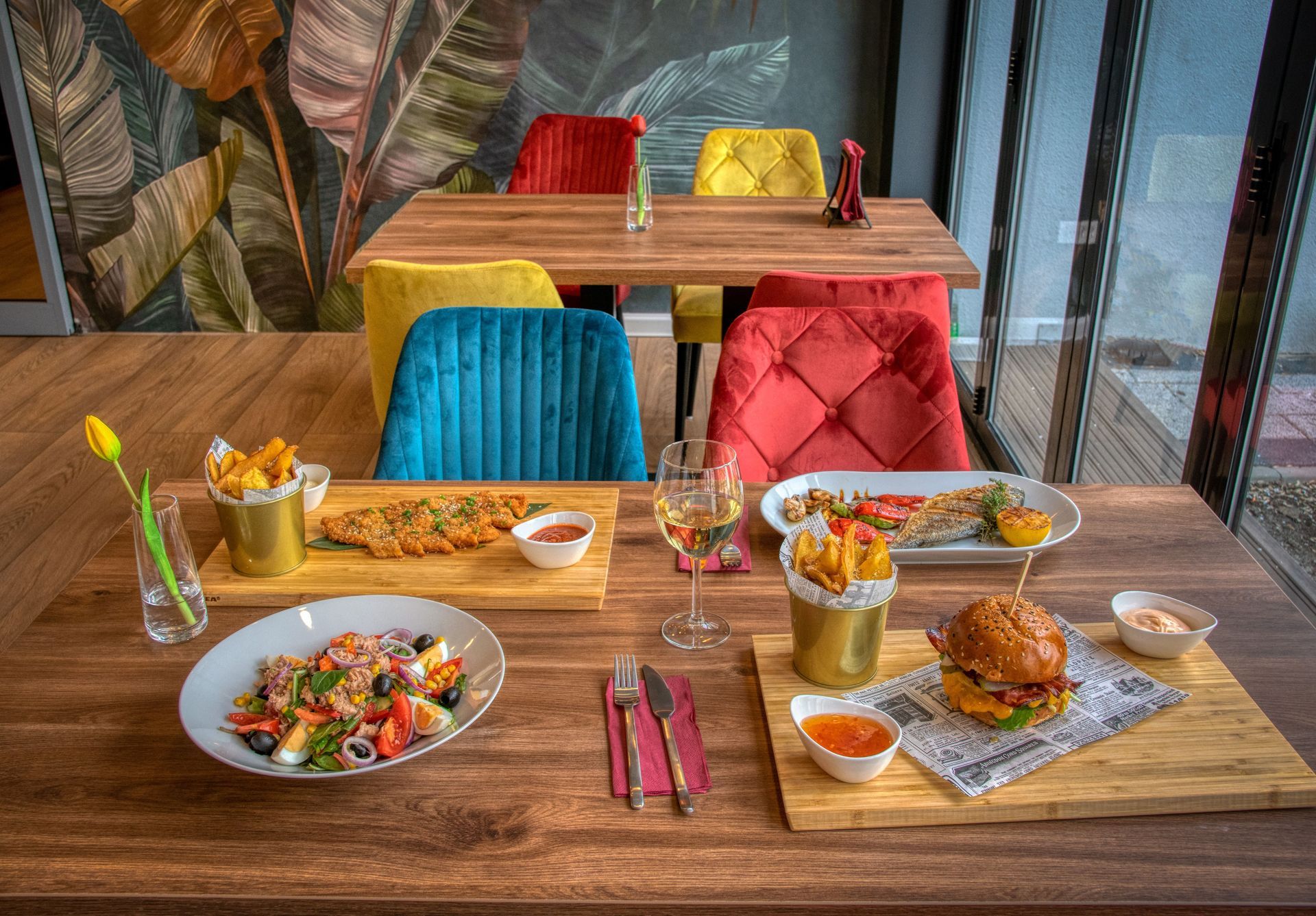 Restaurant table set with colorful chairs and plated meals by large windows