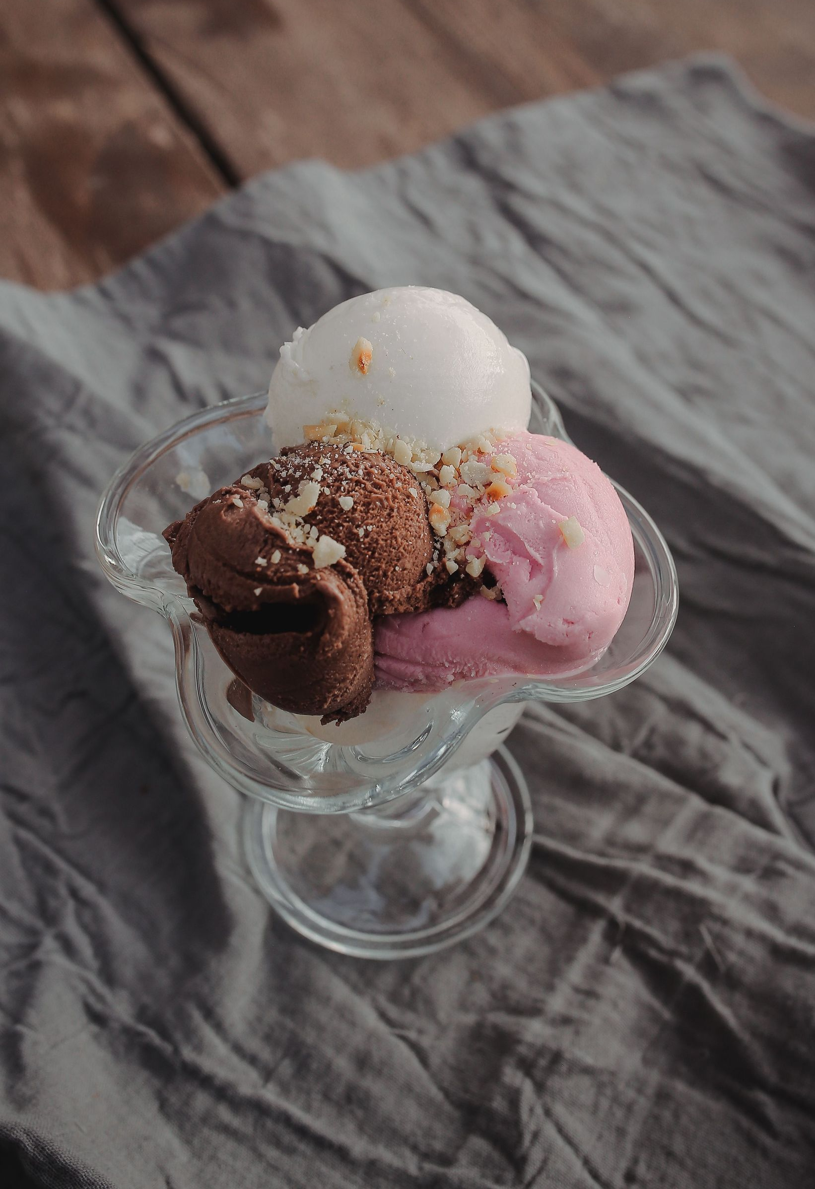 Glass dish with scoops of chocolate, pink, and white ice cream topped with sprinkles on a gray cloth.