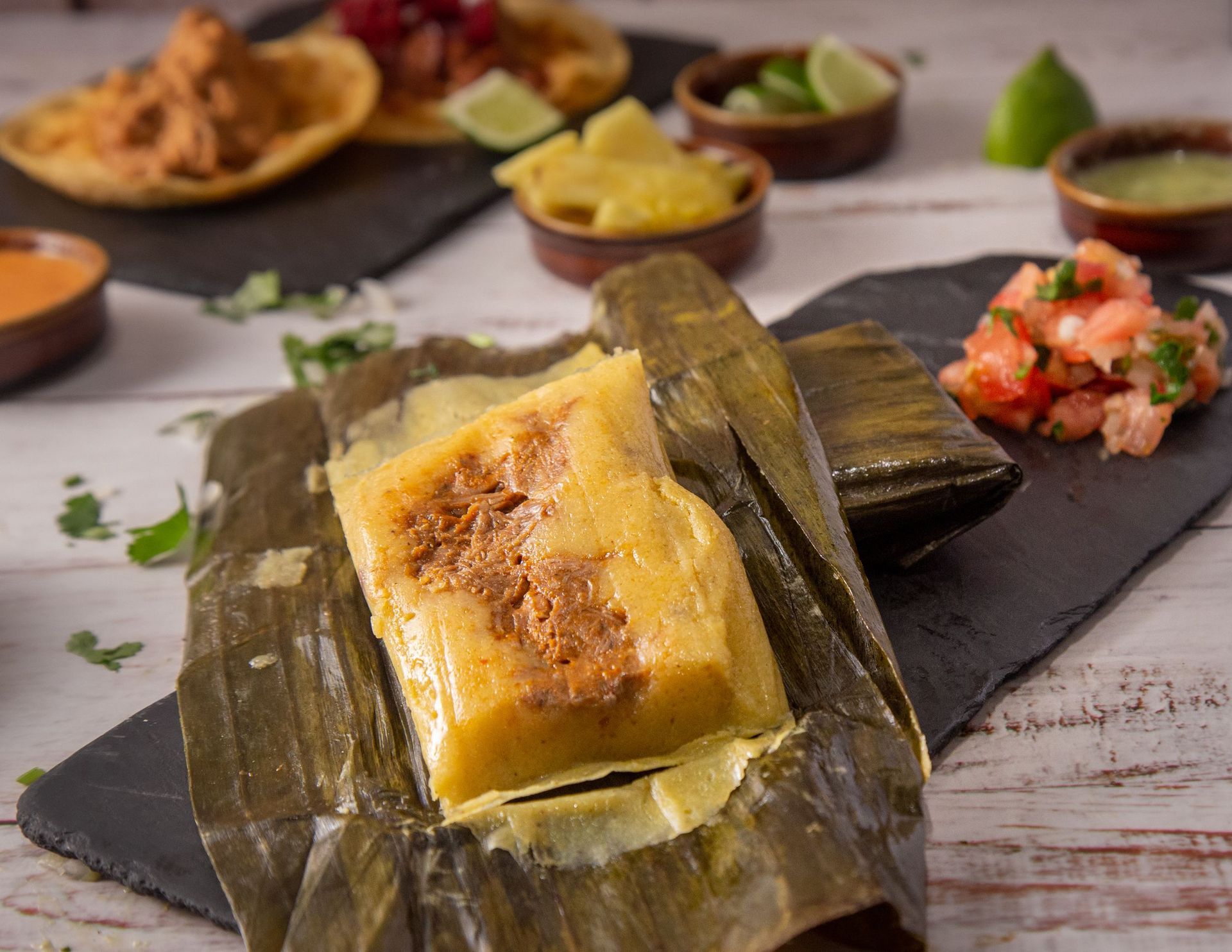 Steamed yellow rice cake on banana leaf with side dishes on a dark plate