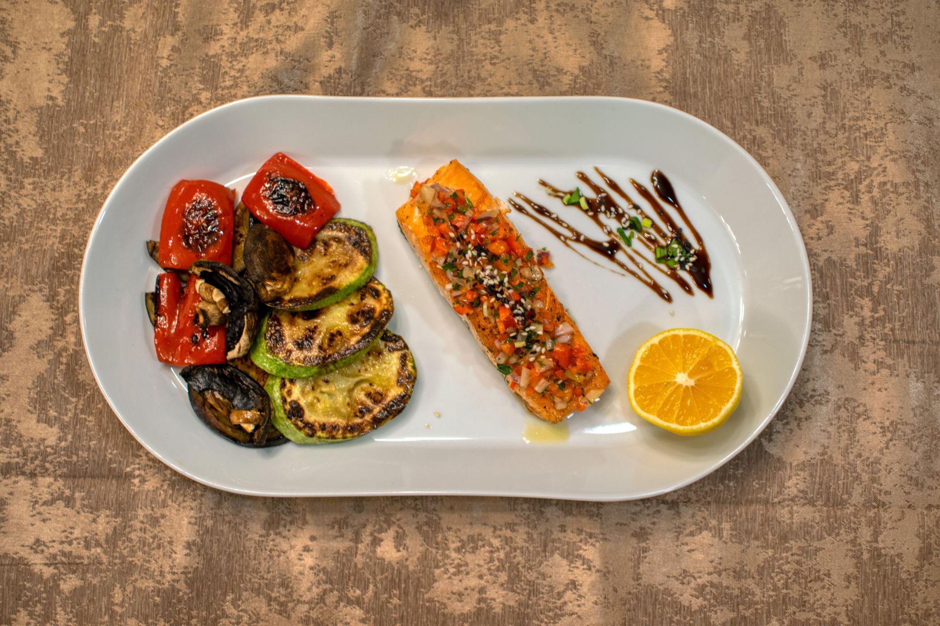 Grilled vegetables, salmon, orange slices, and balsamic drizzle on a white plate