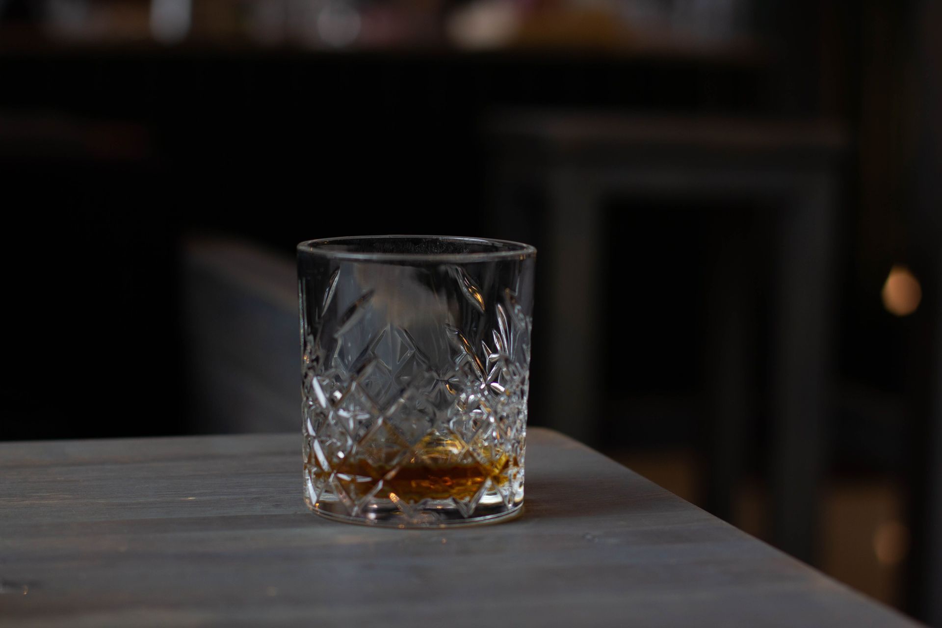 A short tumbler with amber liquor on a dark table in a dim bar setting