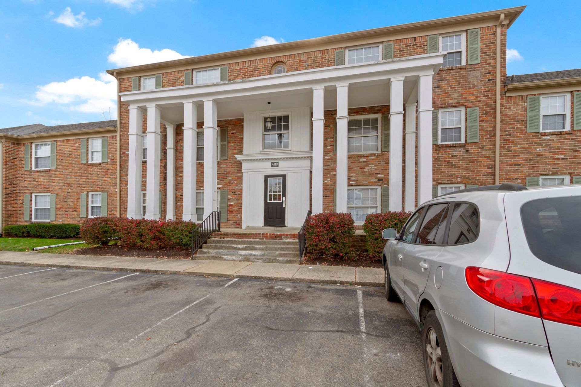 Two-story brick building with white columns, steps, and a parked SUV in front.