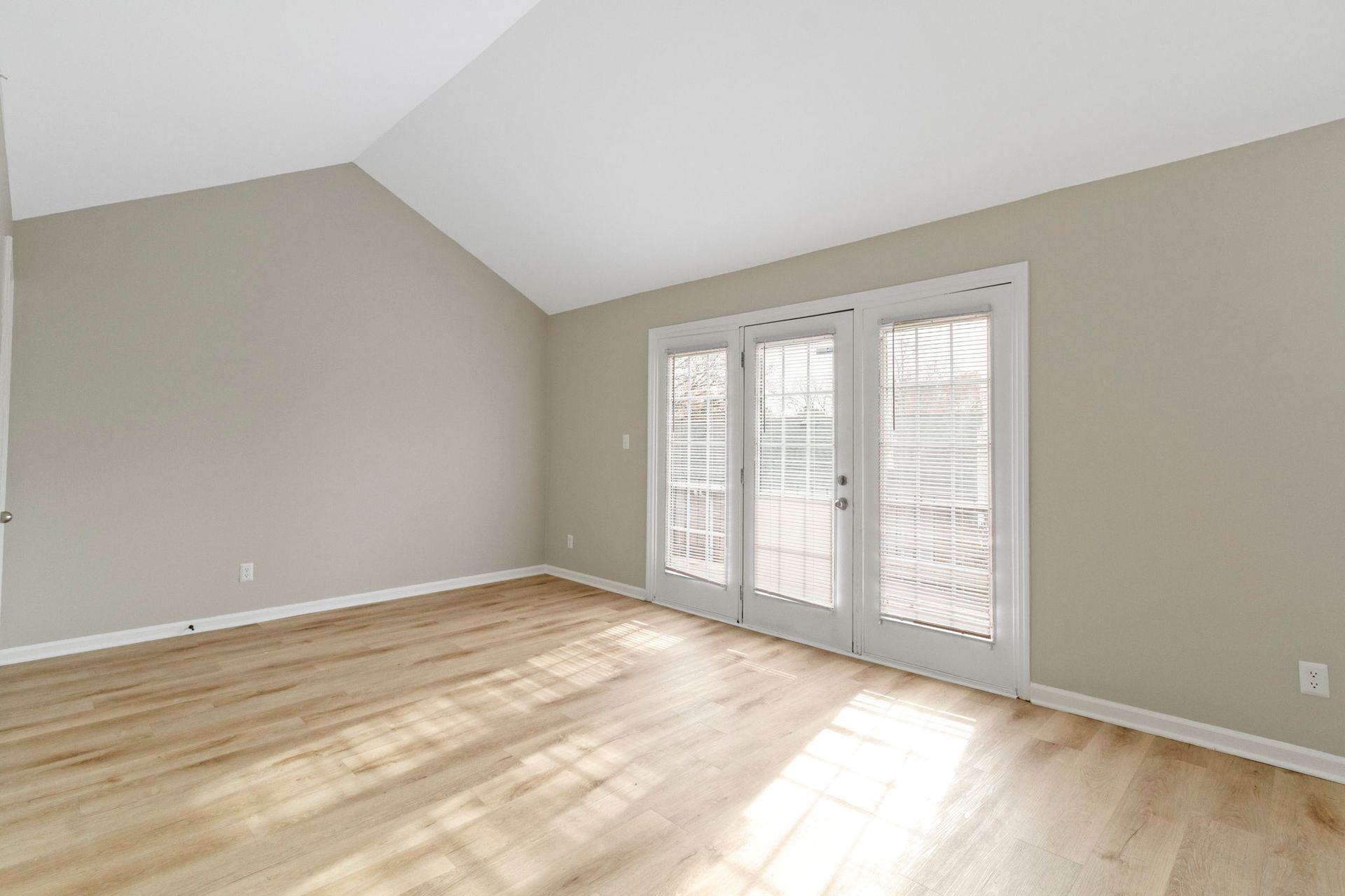 Empty room with hardwood floors, light gray walls, and French doors.