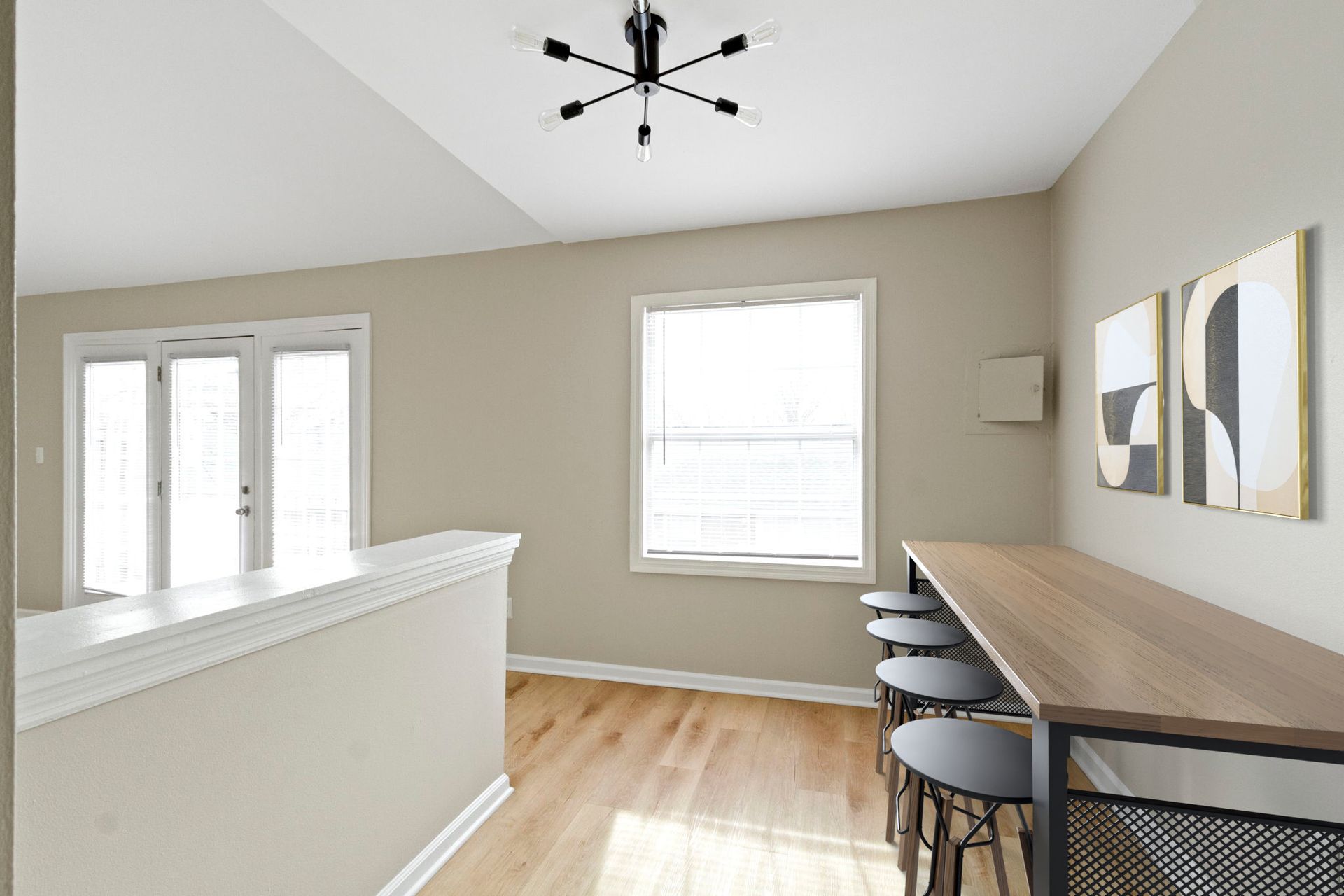 Dining area with a long table, stools, and artwork; light from window and French doors.