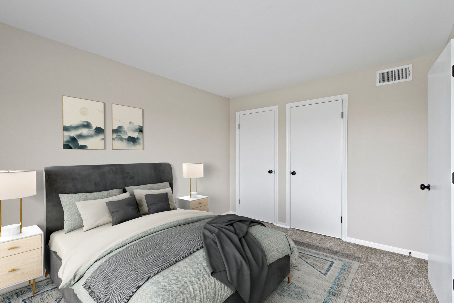 Bedroom with a gray bed, two white doors, neutral walls, and artwork.
