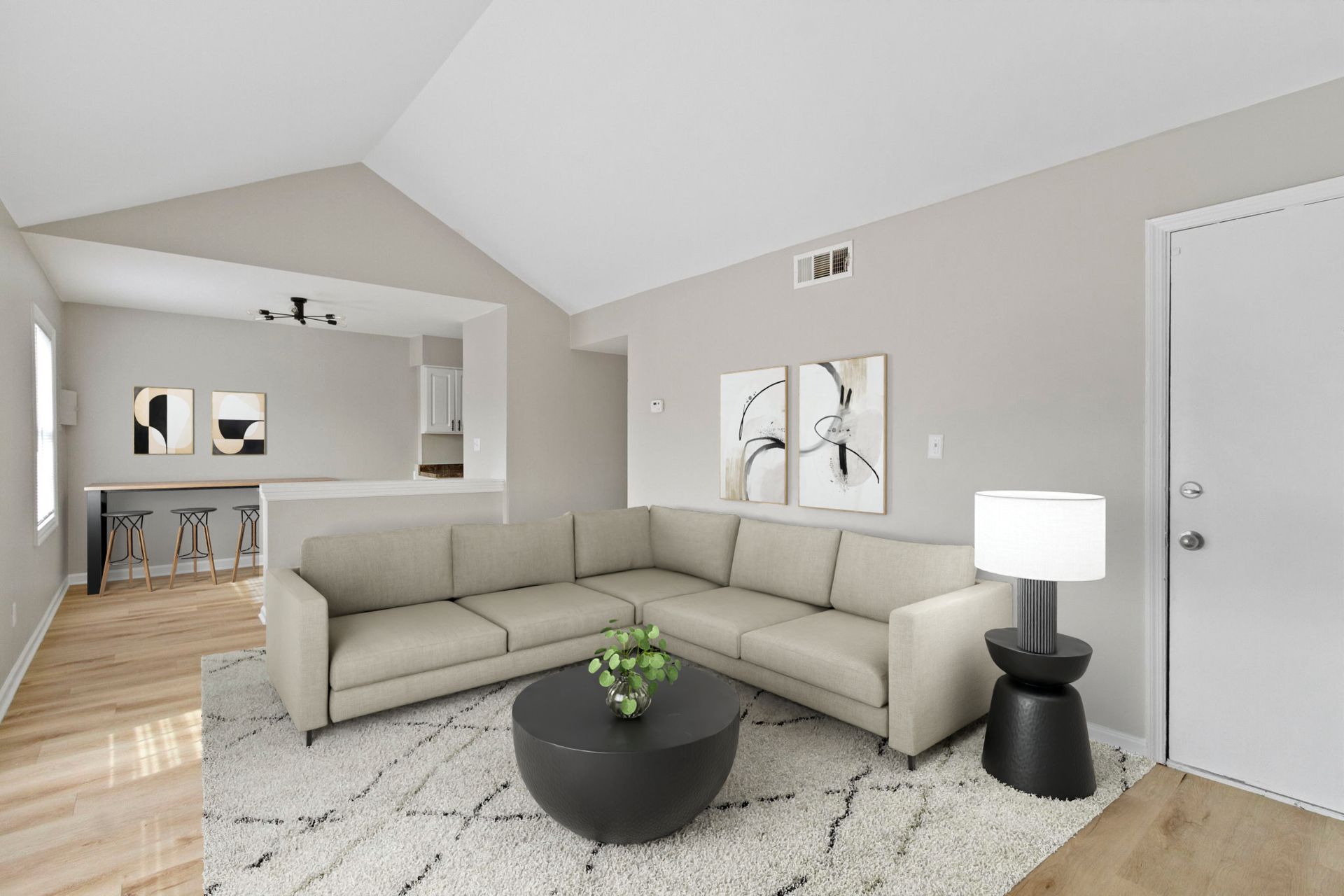 A living room with a light-colored sectional sofa, black coffee table, and artwork.