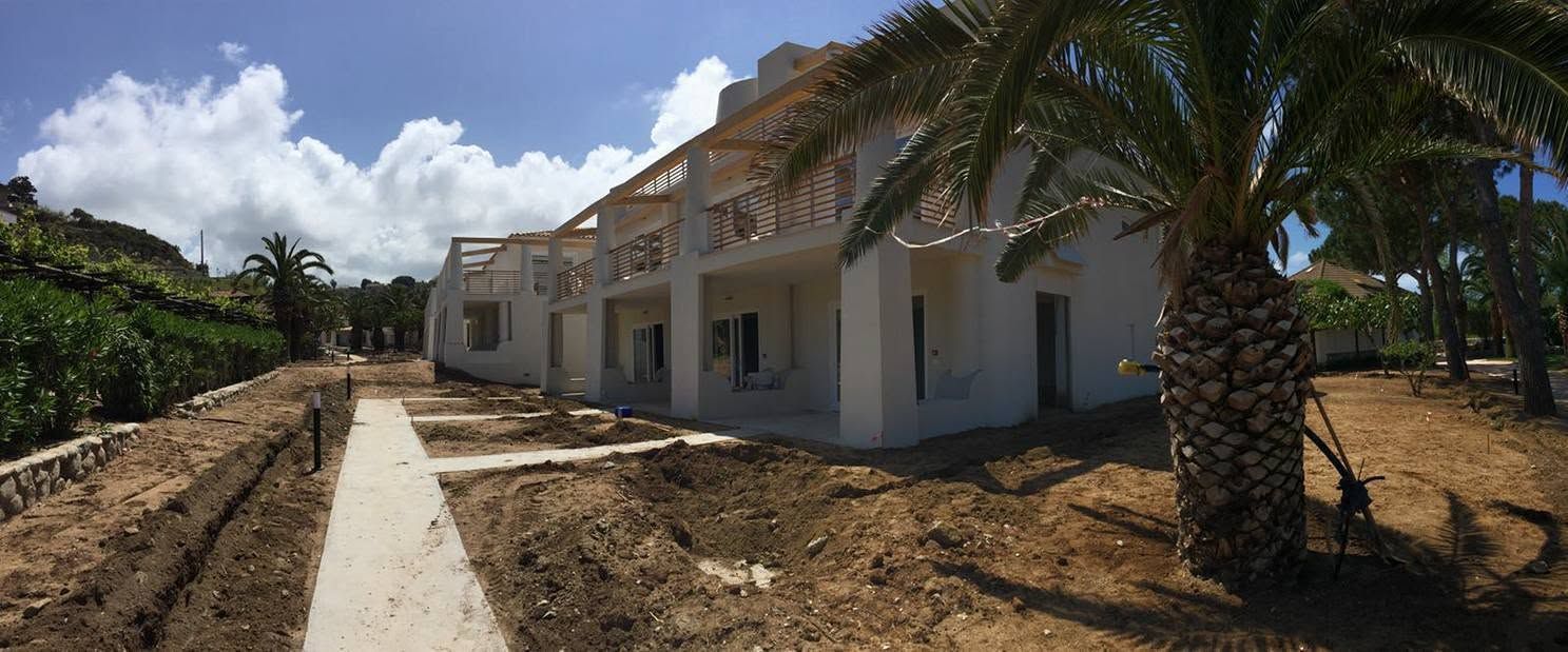 Cantiere edile con fondamenta in cemento, pali in acciaio e un camion sotto un cielo azzurro e limpido.