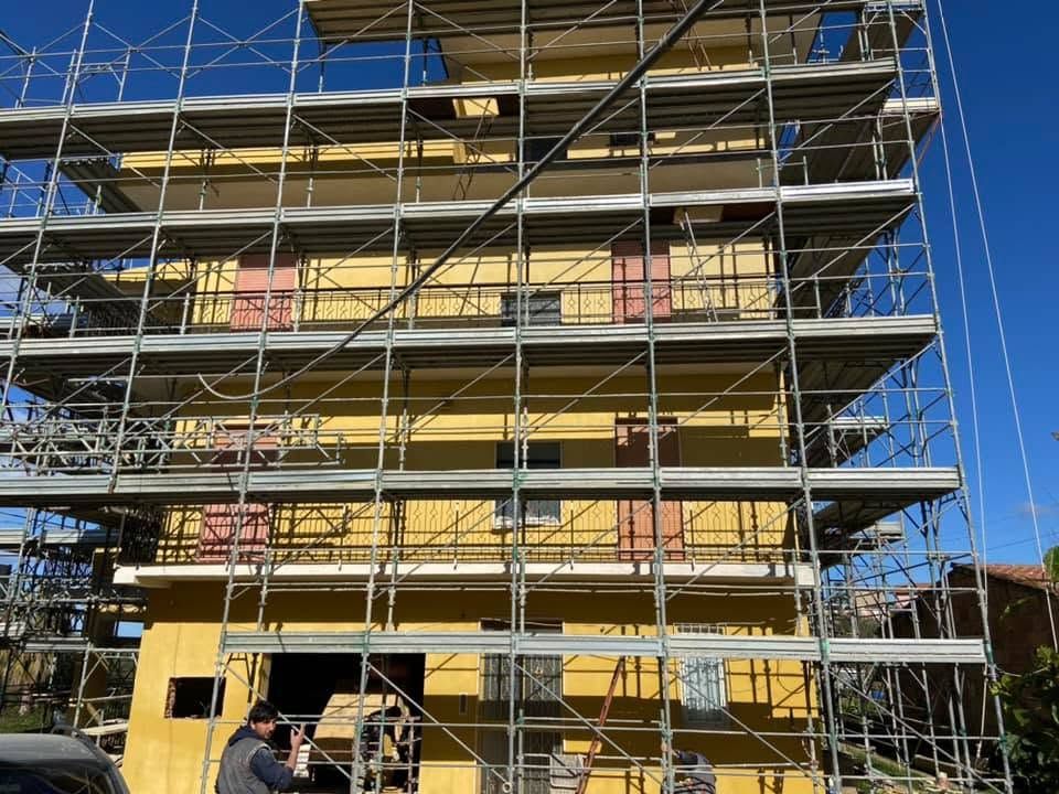 Impalcature che ricoprono un edificio giallo in costruzione sullo sfondo di un cielo azzurro.