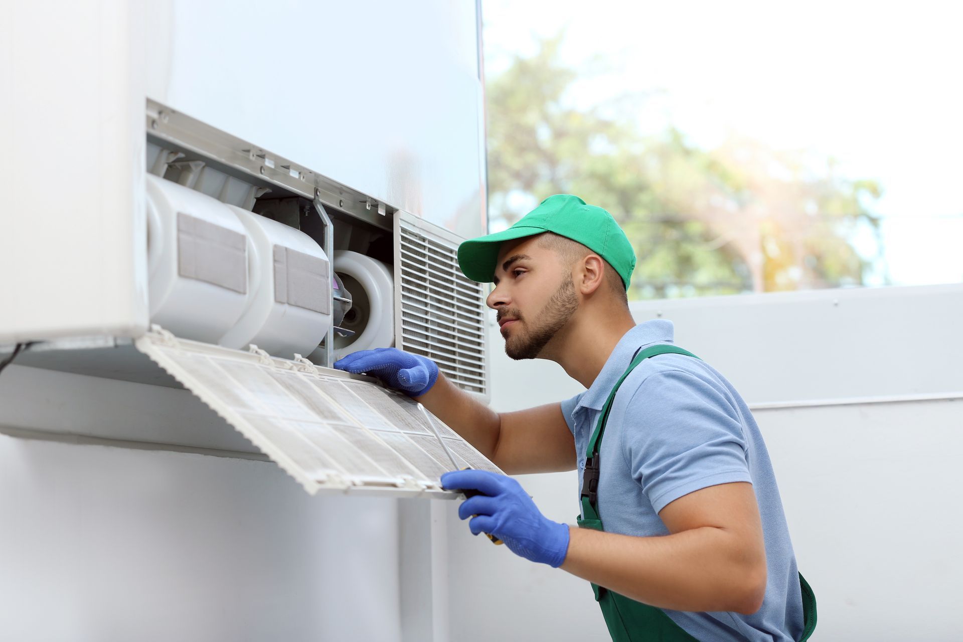 Technician in green cap and gloves cleaning an outdoor air conditioner unit Technician in green cap and gloves cleaning an outdoor air conditioner unit