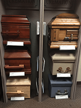 Caskets displayed on shelves in a showroom; various colors and styles.