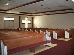 Empty church sanctuary with wooden pews, a cross, and exit doors.