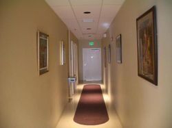 Long hallway with tan walls, dark red runner, artwork, and a closed door at the end.
