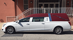 White hearse with burgundy roof parked in front of a building with stairs.