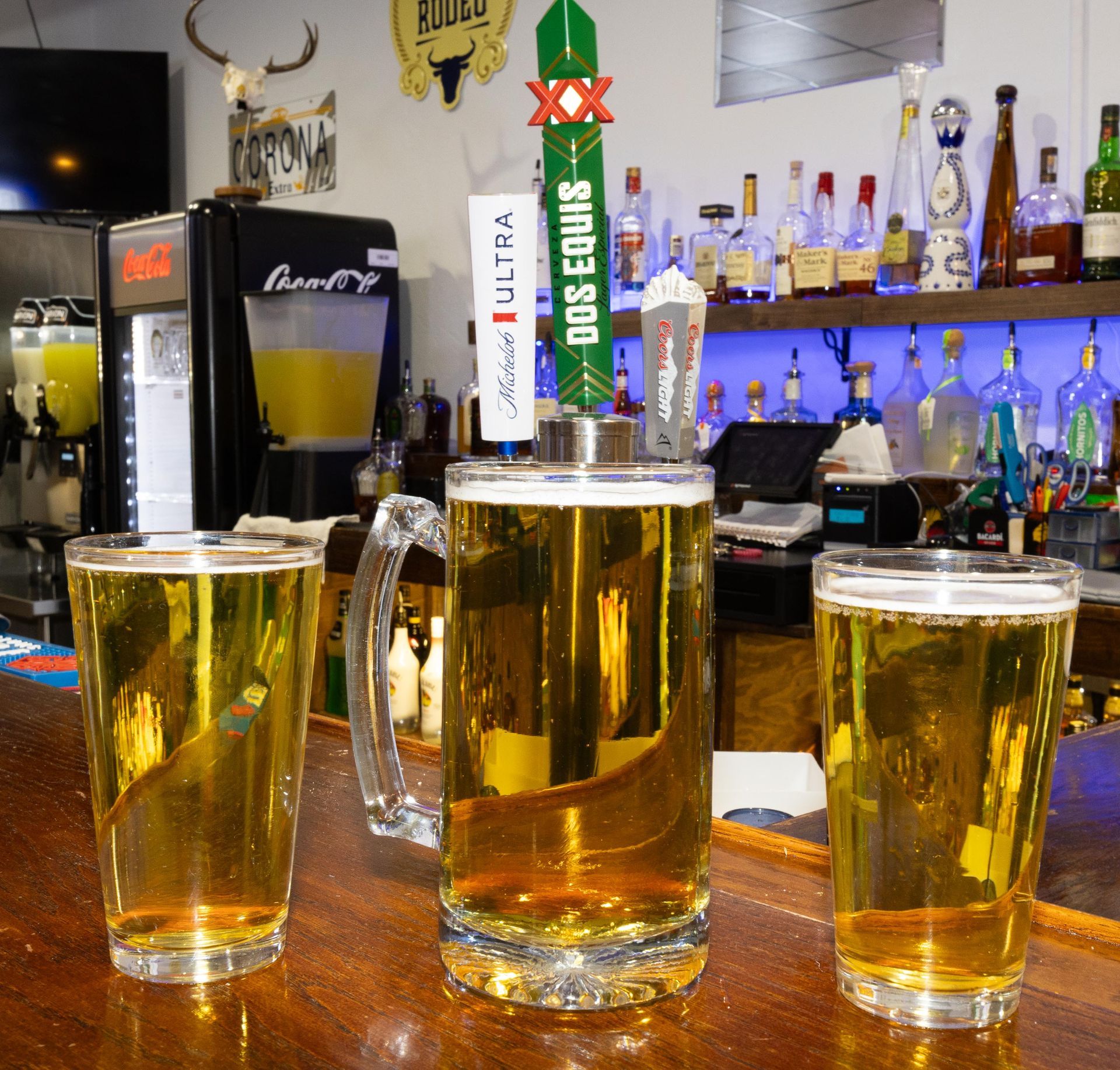 Three glasses of beer on a bar with a dos equis tap