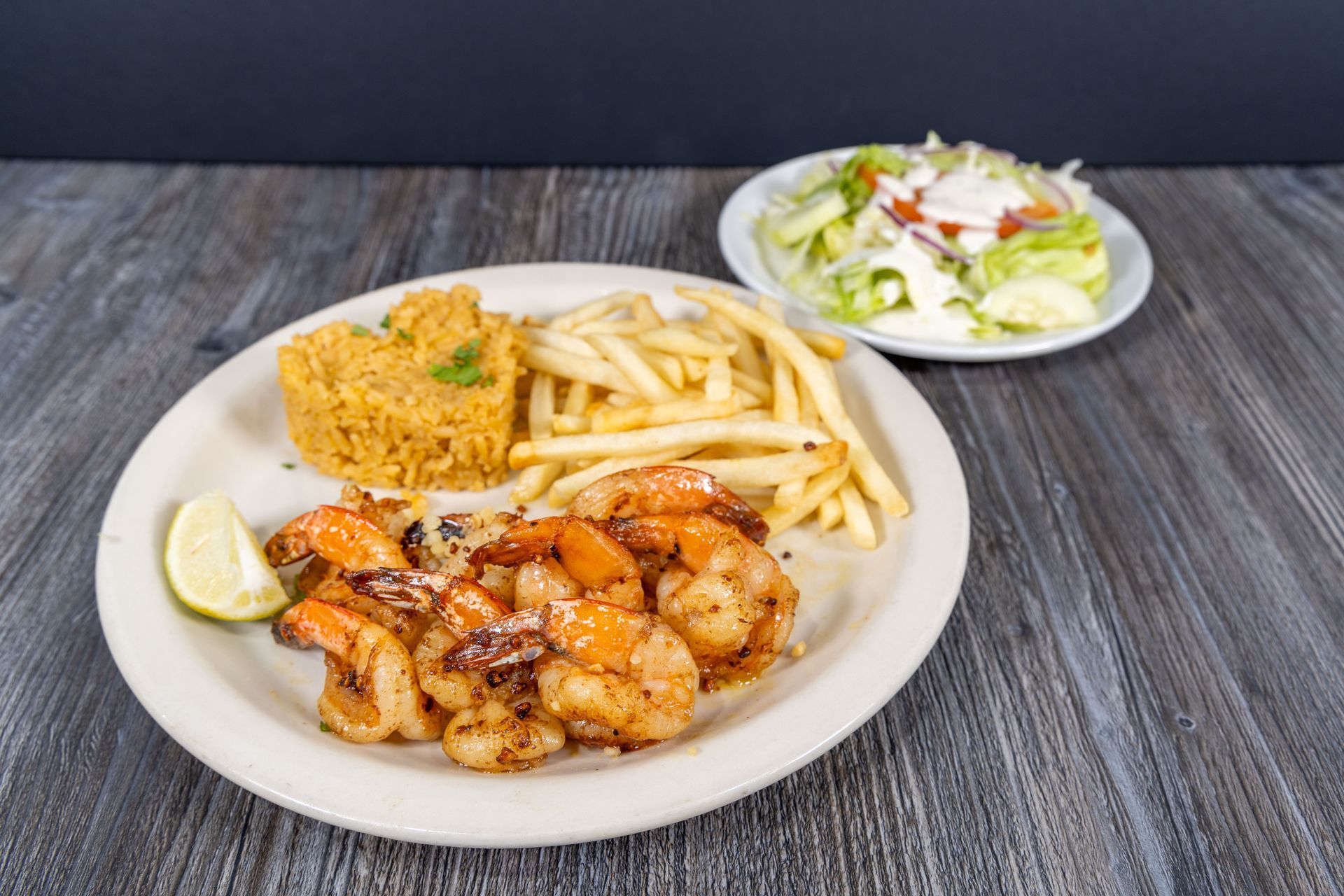 A plate of shrimp , french fries , rice and a salad on a wooden table.