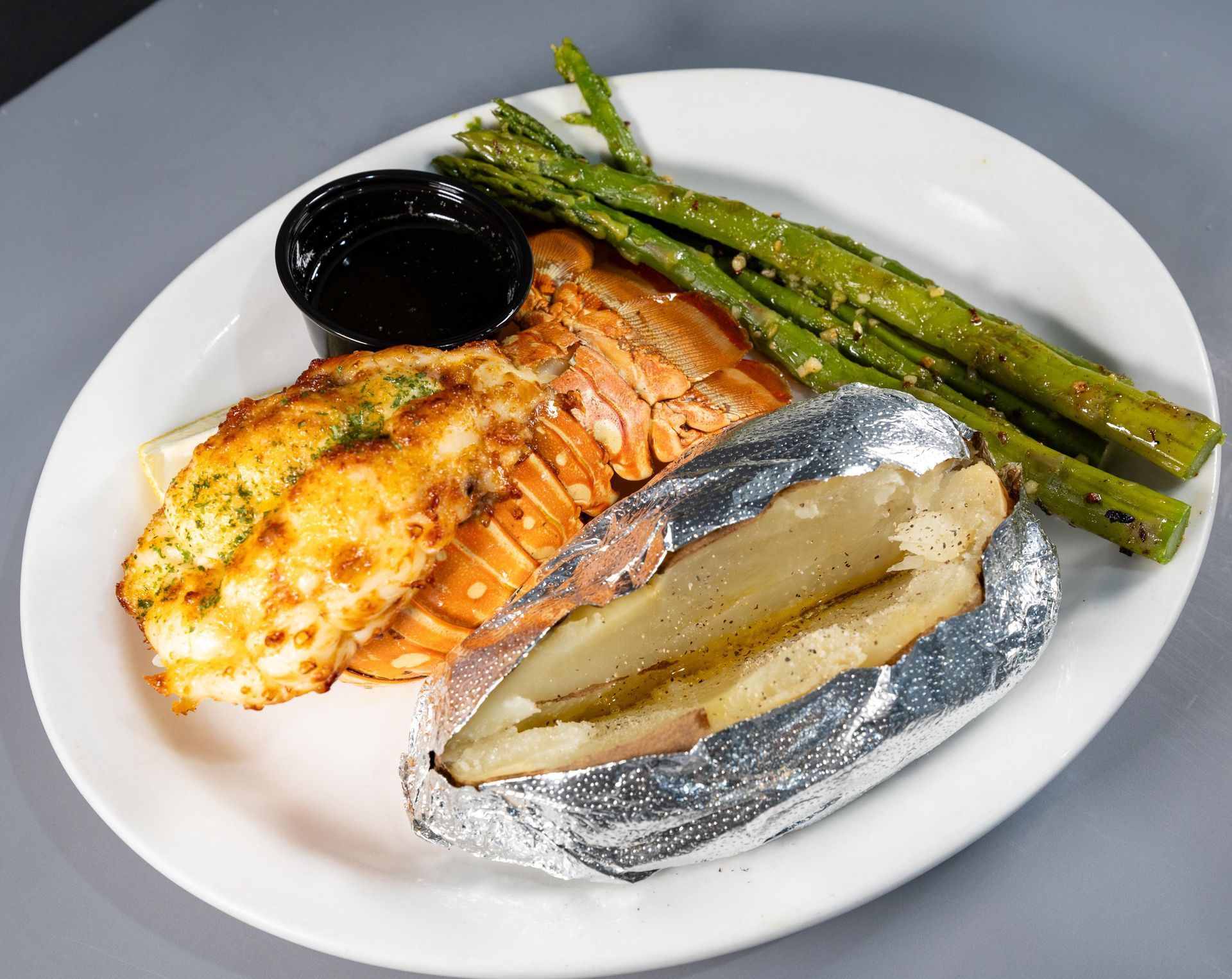 A white plate topped with lobster tail asparagus and a baked potato