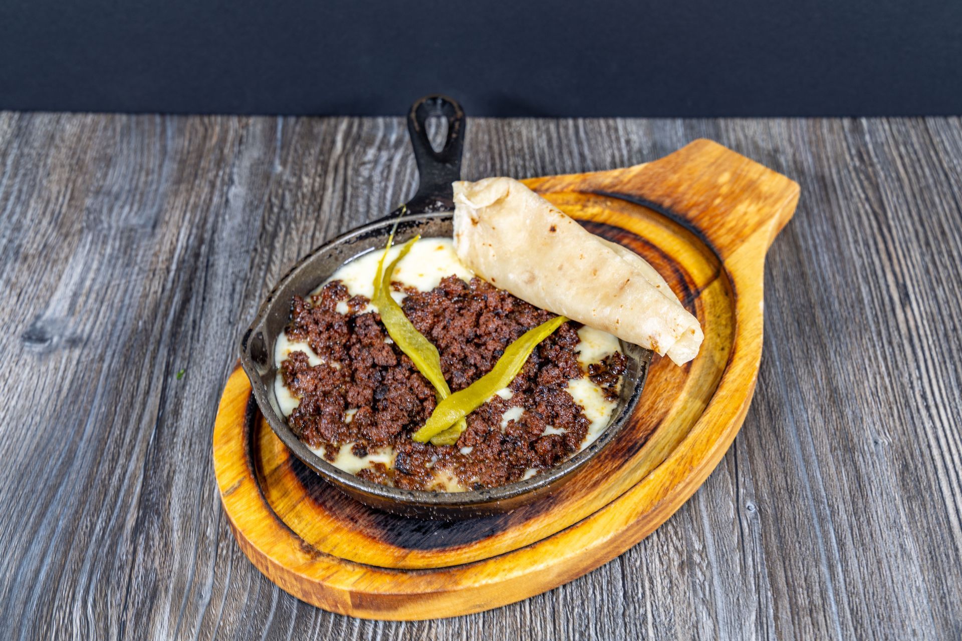 A skillet filled with meat and cheese on a wooden cutting board.