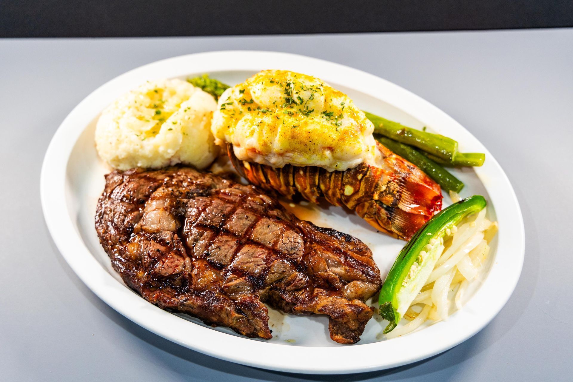 A white plate topped with a steak , lobster tail , mashed potatoes and asparagus.