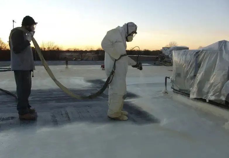 Two men are spraying foam on a roof.