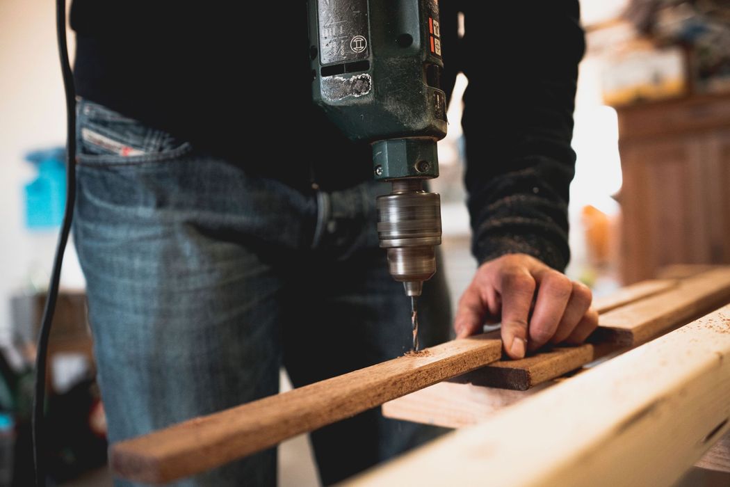 Person drilling a hole in a wooden board in a workshop