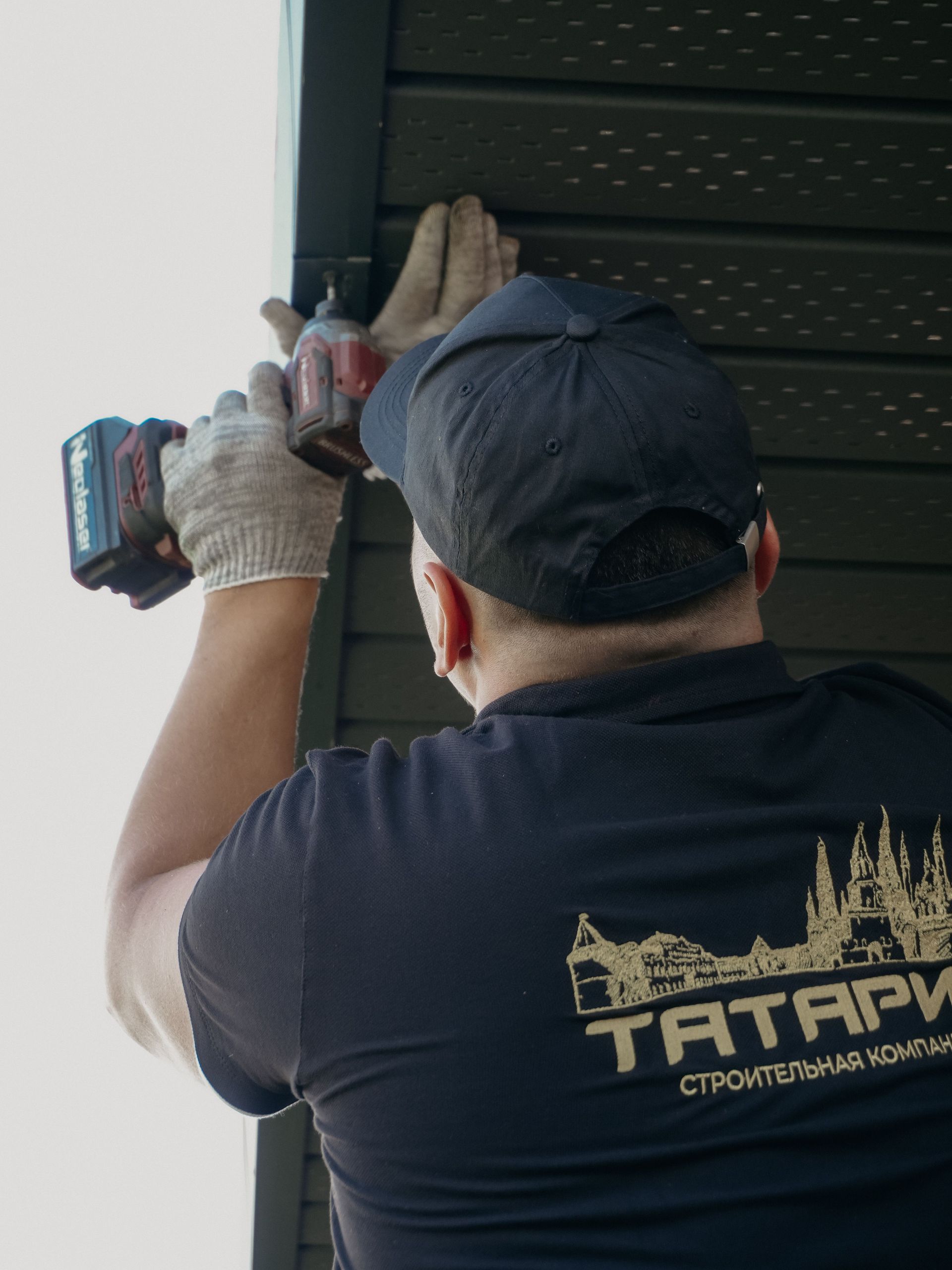 Worker using a drill to install a dark louvered panel on a wall