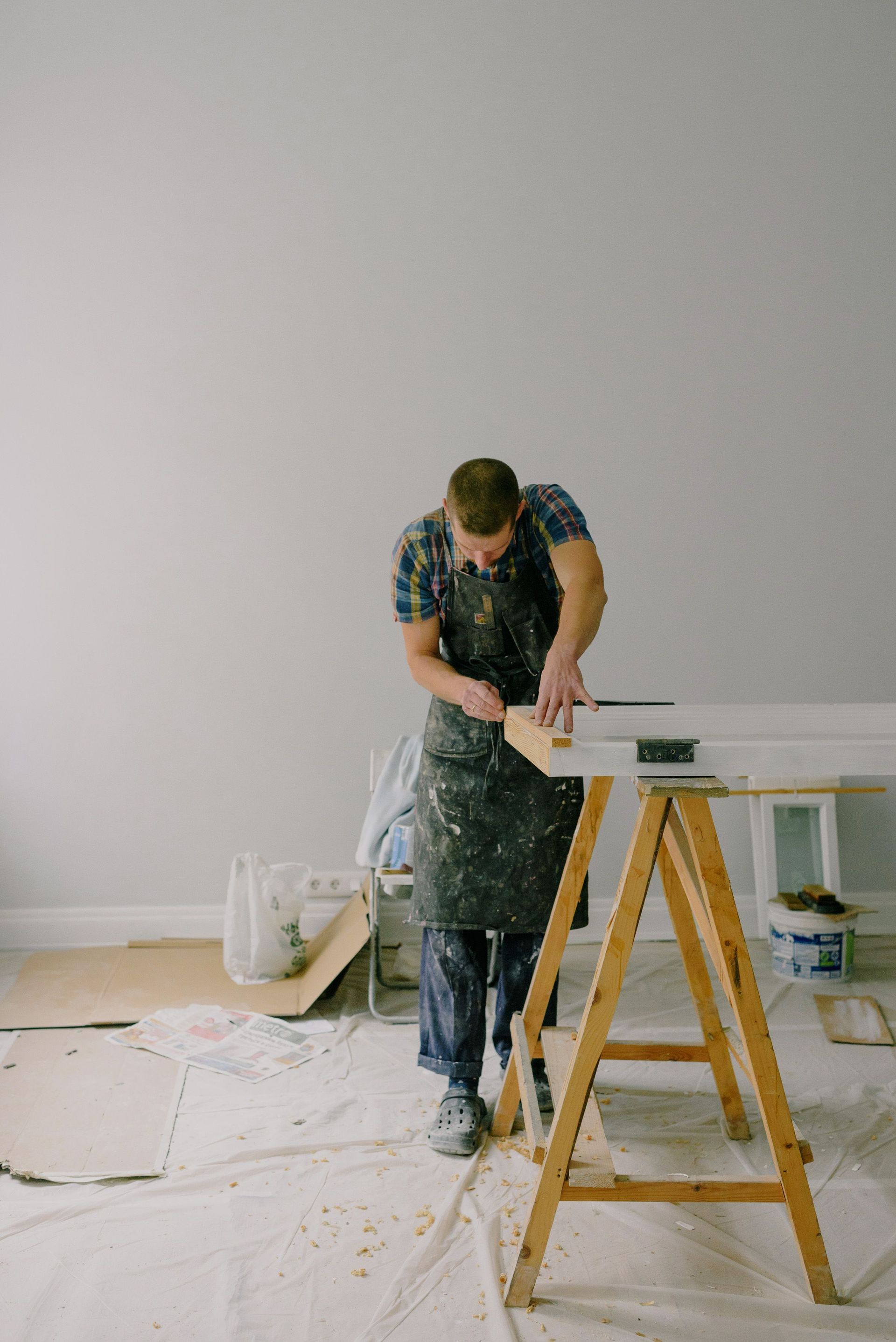 Person sanding a white surface beside a wooden sawhorse in a room under renovation