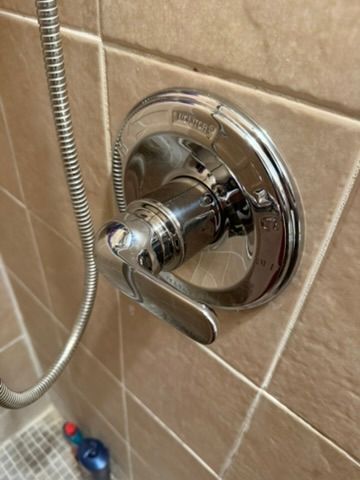 Chrome shower control knob on beige tiled wall with handheld shower hose.