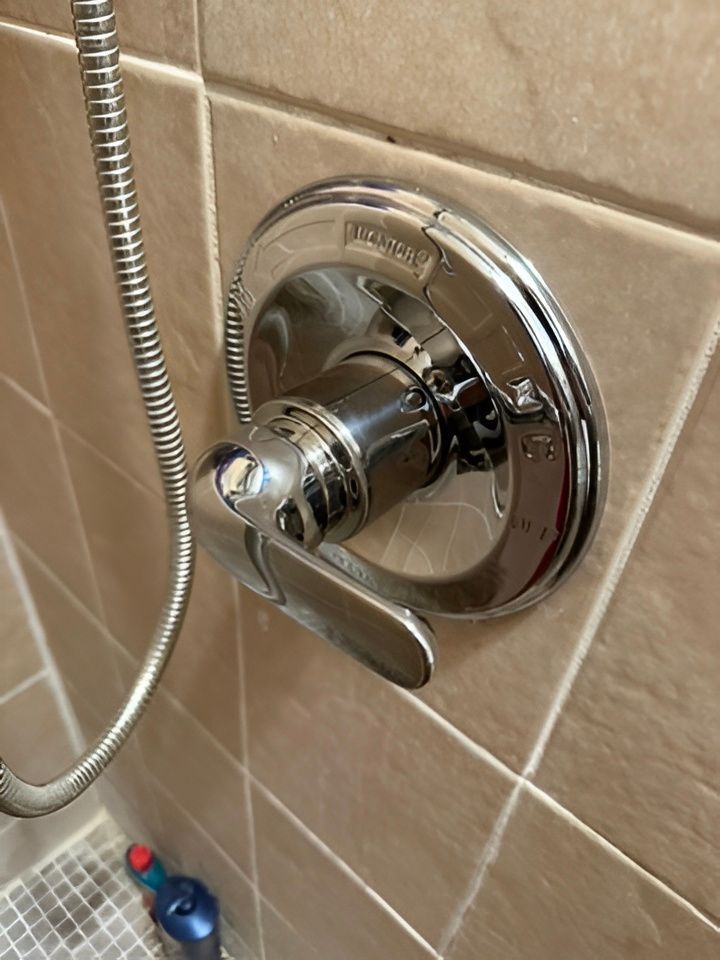 Chrome shower control knob on beige tiled wall with attached handheld shower hose