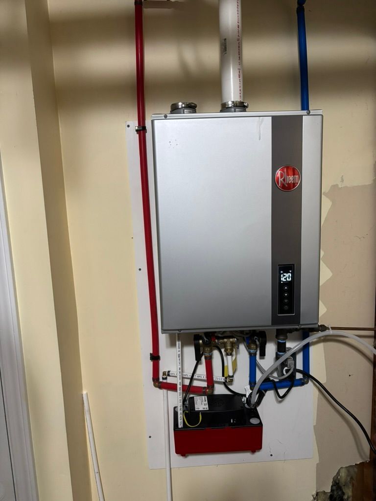Wall-mounted tankless water heater with exposed red and blue pipes and wiring in a utility closet