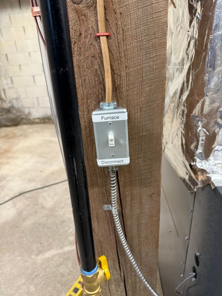 Wall switch mounted on wooden post beside conduit and pipes in an unfinished interior.