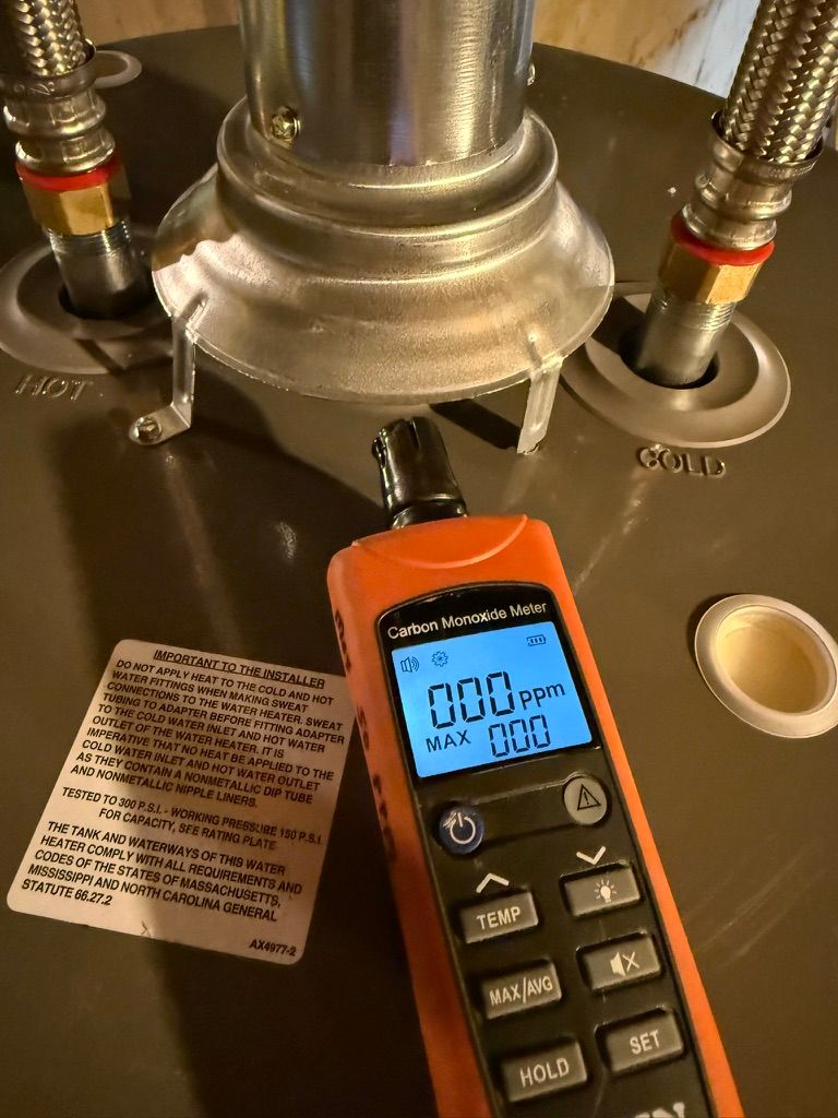 Orange handheld meter attached to a metal pipe under a sink, showing a 0.0 reading.