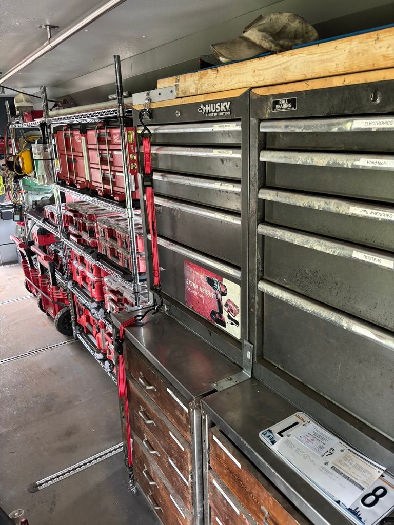 Interior of a work truck with red tool drawers, gray storage bins, and shelves along the side wall