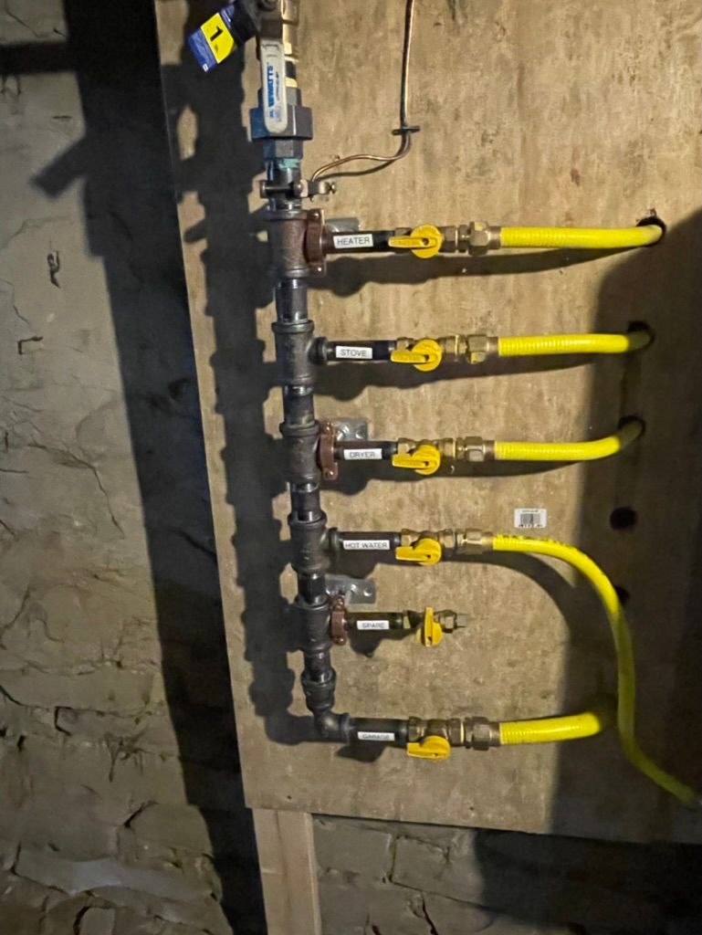 Yellow gas pipes and valves mounted on a wall, with a meter and curved pipe on the right.